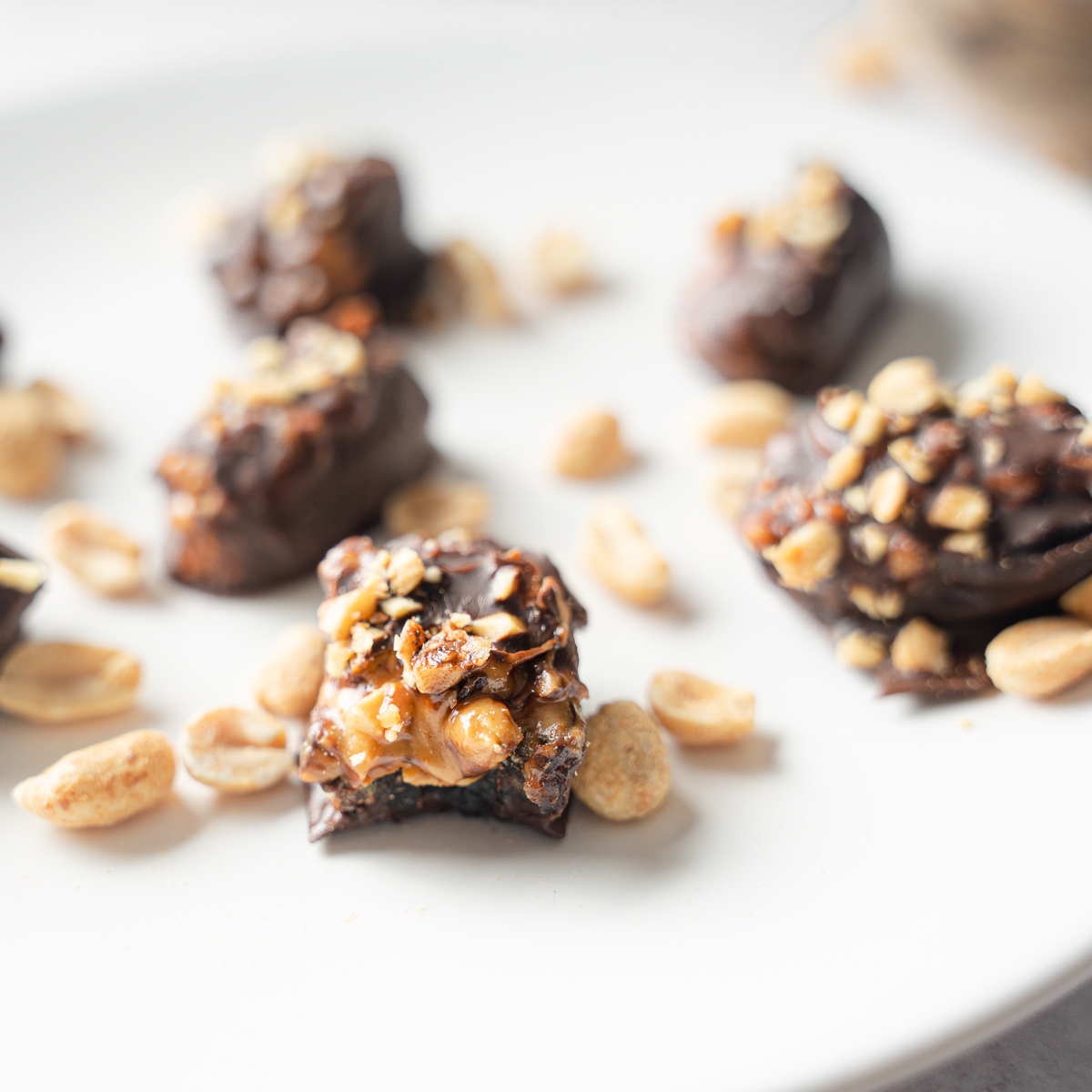 Dates with Peanut Butter with a bite taken out of the center date. Peanuts are scattered over the plate.